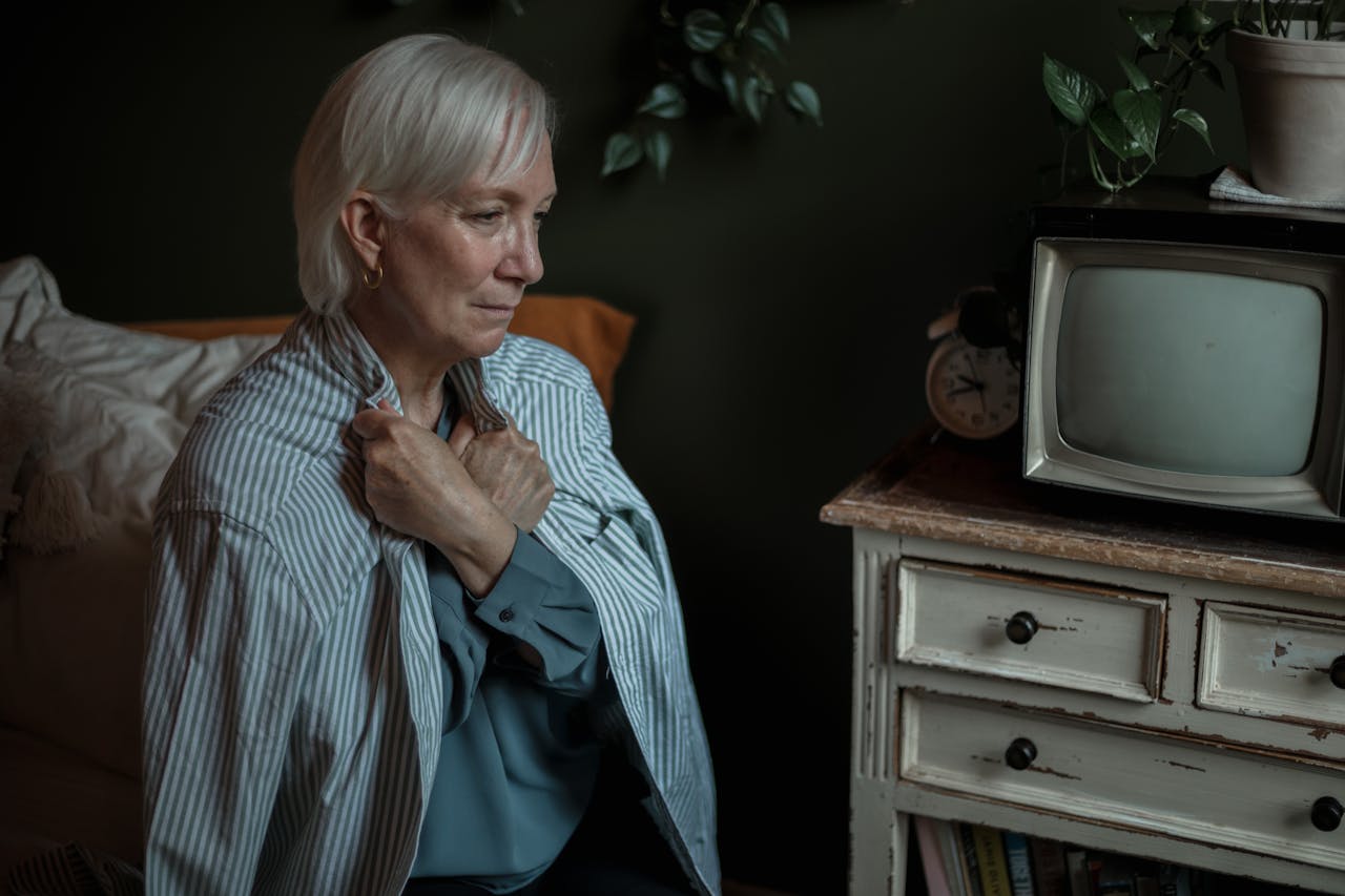 portfolio-05 Elderly woman in a striped shirt sitting thoughtfully indoors, clutching her chest.